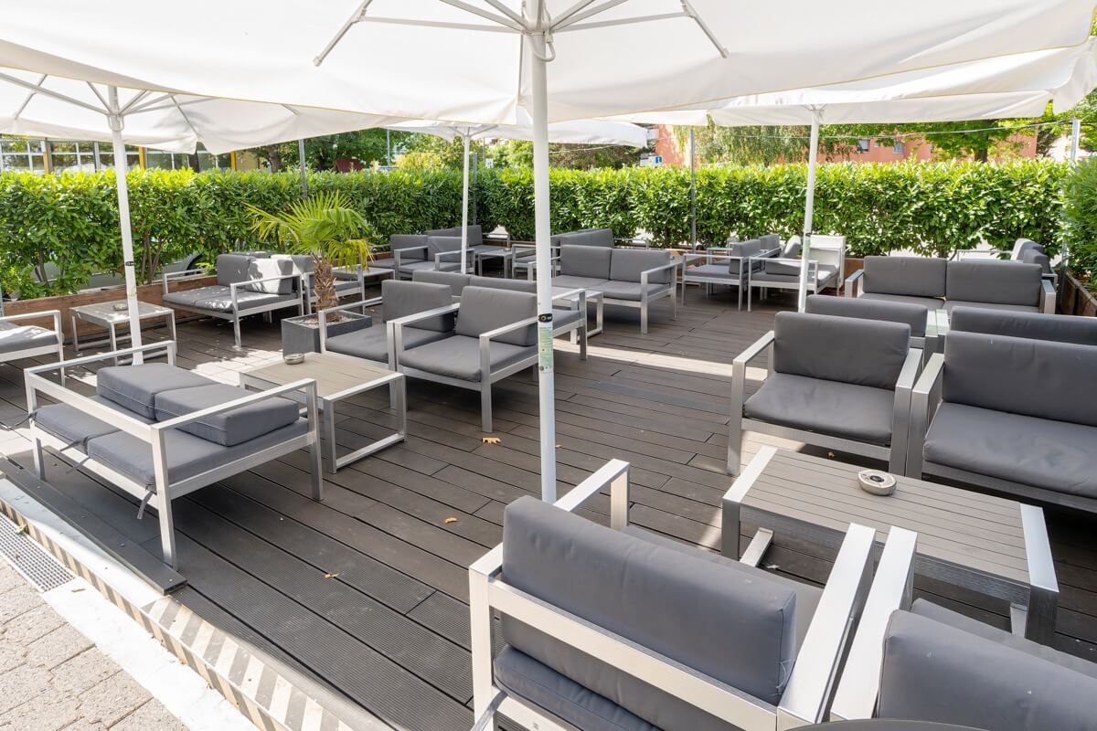 Terrasse lounge du American Pub à Sion avec fauteuils confortables et parasols, idéale pour déguster burgers, bières et cocktails